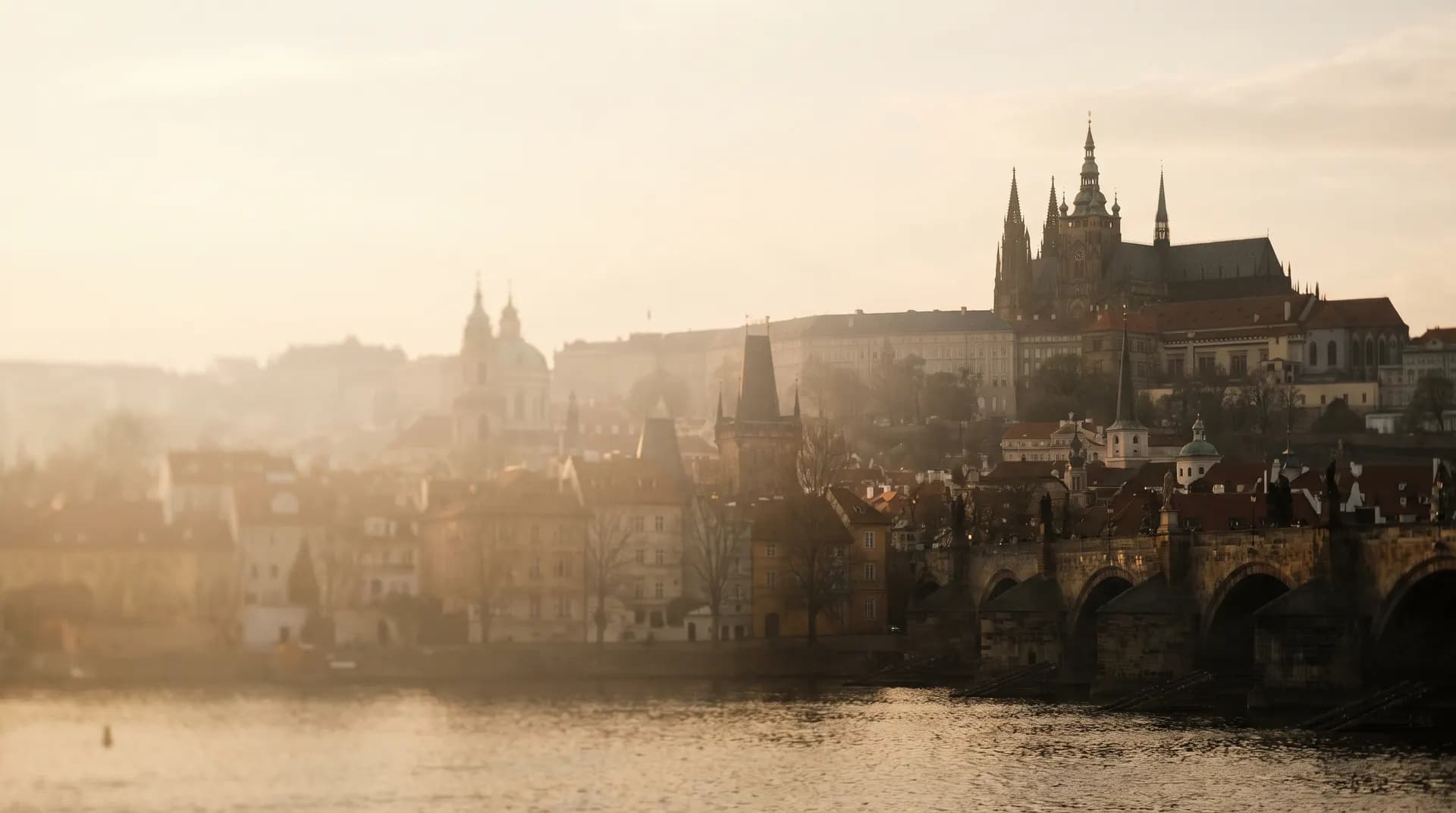Prague Castle and Charles Bridge above the Vltava, veiled in golden-hour haze